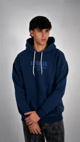 Hoodie azul marino con capucha y cordones blancos, presenta un estampado frontal con el logo de la marca y texto en japonés y la palabra Tokyo.