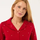 Conjunto de pijama de dos piezas confeccionado en tejido jersey color rojo con estampado de pequeñas cruces blancas. La parte superior consiste en una camisa de manga larga con cuello de solapa y cierre frontal de botones, mientras que la parte inferior es un pantalón largo de corte recto.