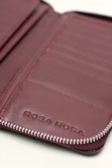Billetera rectangular de cuero con textura de reptil, cierre perimetral y correa de muñeca lateral. Presenta un pequeño aplique metálico circular en el centro.