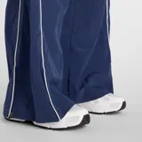 Pantalón deportivo de corte holgado y tiro medio, confeccionado en tejido ripstop de nailon. Presenta un diseño en color azul marino con ribetes laterales en contraste blanco y logo de la marca bordado en la parte superior. Cuenta con cintura elástica y bolsillos laterales.