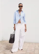 Camisa de corte crop y diseño recto, con estampado de rayas verticales en azul y blanco. Presenta cuello camisero, bolsillo en el pecho, cierre frontal con botones y mangas tres cuartos.