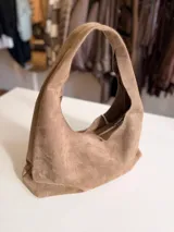 Cartera tipo hobo de diseño flexible y caída natural, confeccionada en material con textura simil gamuza. Cuenta con asa corta integrada para llevar al hombro, cierre superior y bolsillo interior con cierre.