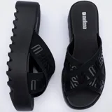 Sandalias Melissa modelo Cozy Slide de color negro, con plataforma gruesa dentada y tiras cruzadas de tela con el logotipo de la marca.