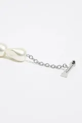 Pulsera de cadena metálica plateada combinada con perlas sintéticas irregulares, cierre tipo T y dijes colgantes en forma de corazón, uno de metal liso y otro esmaltado en negro con el logo de la marca.