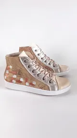 Botas de caña alta de cuero vacuno en color beige con brillo leve, detalles metálicos plateados y diseño artístico pintado a mano en el talón. Cuenta con cordones y suela de goma blanca.