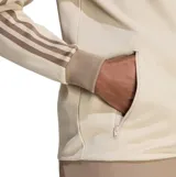Campera deportiva Adidas modelo Beckenbauer, de color beige con las icónicas tres tiras en tono tostado en las mangas. Presenta cuello alto, cierre frontal completo y bolsillos laterales con cierre.