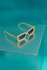 Lentes de sol con armazón rectangular de color amarillo traslúcido y cristales oscuros con protección UV.