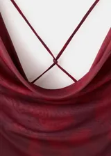 Vestido largo rojo con estampado abstracto en tonos oscuros, escote drapeado, sin mangas y silueta ajustada.