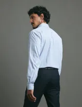 Camisa de vestir de manga larga con diseño de rayas verticales en tonos blanco y celeste. Presenta cuello clásico, cierre frontal con botones y un bolsillo en el pecho.