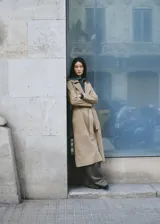 Gabardina larga de piel caprina en color beige, con solapas amplias, cierre cruzado con botones y cinturón ajustable del mismo material.