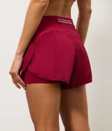 Short runner deportivo 2x1 de microfibra color bordó, con cintura elástica, bolsillo funcional con cierre y bajo redondeado.