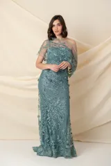 Vestido largo de fiesta color verde agua, confeccionado en tul bordado con apliques florales. Diseño strapless con escote asimétrico y capa de tul bordado sobre un hombro. Incluye cinto con strass y piedras. Ideal para madrinas o madres de quinceañeras.