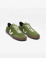 Championes Veja modelo Panenka, confeccionados en gamuza color verde oliva. Presentan el logo lateral en forma de V en color crema, suela de goma marrón y detalle en el talón con el nombre de la marca.