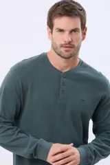 Remera de algodón texturada color gris oscuro, de manga larga, con cuello redondo y botones en la parte frontal. Presenta un pequeño logo bordado en el pecho y un parche decorativo en la manga izquierda.