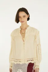 Blusa de mangas largas con puños abotonados, cuello alto con detalles de encaje y cierre frontal de botones forrados, confeccionada en tejido liviano con aplicaciones caladas.