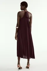 Vestido midi plisado color bordó, con cuello halter, broche de flor en el delantero y anudado en la espalda. Cuenta con forro interior.