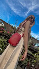 Bandolera compacta color rojo con textura de cuero, correa regulable y desmontable con diseño de rayas rojas y blancas. Cuenta con bolsillos frontales y cierre, interior forrado en tela.