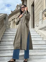 Tapado largo de paño liviano con diseño de cuadros en tonos marrones. Presenta solapas clásicas, bolsillos laterales con detalles en cuero y tajos profundos en los costados.