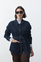 Sobrecamisa de jean color negro con silueta relajada, cuello camisero, cierre frontal con botones metálicos, bolsillos frontales y cinturón ajustable en la cintura.