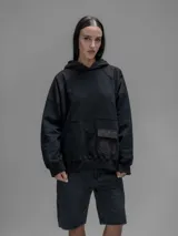 Hoodie oversize color negro, confeccionado en frisa gamuzada de algodón con recortes en hombros y bolsillo frontal tipo cargo con solapa en material técnico. Presenta capucha forrada y puños y ruedo acanalados.