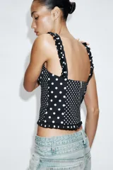 Top estilo corset con escote corazón, tirantes anchos con detalle de fruncido y cierre posterior con cremallera. Presenta un diseño de estampado de lunares en contraste.