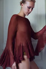 Camisa semitransparente de georgette en color burdeos, con cuello redondo, manga larga asimétrica y detalle de volantes en el bajo. Cuenta con cierre frontal mediante botones.