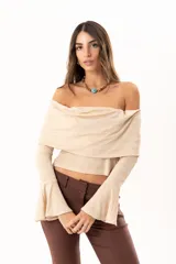 Blusa beige con hombros descubiertos, confeccionada en tela elástica con destellos de lurex. Presenta mangas largas con terminación acampanada y diseño ajustado al cuerpo.
