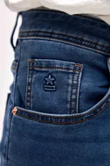 Jean de corte slim, color azul medio, con diseño clásico de cinco bolsillos, cierre frontal con botón y cremallera.