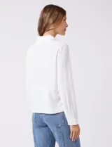 Camisa de crepe color beige con cuello clásico, cierre frontal con botones y dos bolsillos aplicados en el pecho.