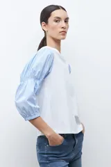 Remera de algodón con cuerpo liso en color blanco y mangas abullonadas de tela camisera con estampado de rayas finas en azul y blanco.