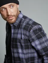 Camisa de manga larga confeccionada en franela de algodón, con diseño de cuadros en tonos marrones, mostaza y blanco. Presenta cuello con botones, cierre frontal abotonado y bolsillo en el pecho.