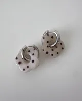 Aros de acero quirúrgico con argolla plateada y dije de flor translúcida en color lila con lunares negros.