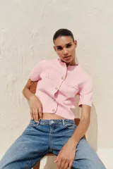 Chaqueta de punto color amarillo pálido, con cuello redondo, manga corta, cierre frontal con botones dorados y bolsillos de parche en el pecho.