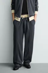 Pantalón jogger de corte wide fit en tejido compacto color gris oscuro. Presenta cintura elástica con cordón ajustable, bandas laterales en contraste color beige y costuras frontales tipo pinza.