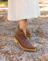 Botín de cuero vacuno color marrón oscuro, con taco de madera foliado en cuero de 5cm de altura, cierre lateral interno y horma de punta fina.