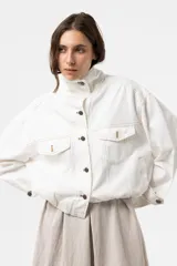 Campera de denim liviano oversize color blanco, con cuello alto, cierre frontal con botones y bolsillos delanteros con solapa. Presenta pespuntes en contraste y una silueta relajada.