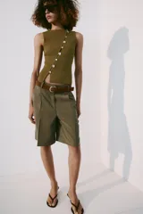 Top de punto color verde oliva, sin mangas, con cuello redondo y diseño ajustado. Presenta una hilera diagonal de botones nacarados en el frente.