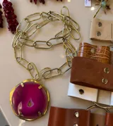 Collar de cadena larga de eslabones dorados con un dije circular de piedra ágata en color fucsia engarzada en bronce.