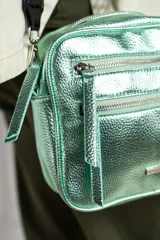 Cartera bandolera rectangular color oro viejo, con textura granulada y correa ancha de tela negra regulable. Tiene dos bolsillos frontales con cierre y un bolsillo interno.