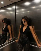 Catsuit de encaje negro con diseño de cuerpo entero, escote profundo en V y estilo halter. Presenta una textura floral detallada en todo el tejido.