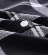 Camisa de franela de manga larga con estampado de cuadros en blanco y negro. Presenta cuello inglés, cierre frontal con botones y bolsillo en el pecho.