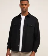 Camisa negra de manga larga confeccionada en sarga de algodón, con cuello inglés, bolsillos con solapa en el pecho y cierre frontal de botones a presión.