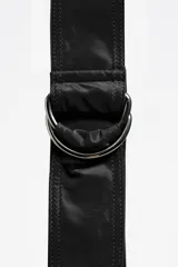 Bolso tipo media luna (hobo bag) de nylon negro, con costuras verticales que le dan estructura y un asa de hombro ajustable con hebilla metálica. Presenta el logo de Bimba y Lola en blanco en la parte inferior central.