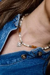 Collar de cuentas de piedra natural en tonos crema y marrón, intercaladas con separadores metálicos plateados y un dije central con forma de punta de flecha en metal plateado.
