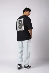 Remera negra de corte oversize confeccionada en tela pesada. Presenta un bordado frontal con la palabra 'REWIND' y un diseño de parche en la espalda con estética de papel roto.
