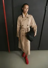 Gabardina larga color beige, de doble botonadura, con solapas amplias, mangas largas raglán, cinturón ajustable con hebilla y bolsillos laterales.