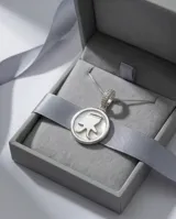 Dije circular de plata 925 con centro de nácar y silueta de niño en relieve. El pasante está decorado con circonias brillantes y se presenta con una cadena de plata fina.