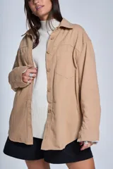 Sobrecamisa color beige confeccionada en gabardina, de corte holgado, con cuello camisero, cierre frontal con botones, dos bolsillos de parche en el pecho y mangas largas con puños abotonados.