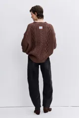 Sweater de punto color blanco off-white, con cuello redondo y diseño texturizado con trenzas y pompones en el frente.