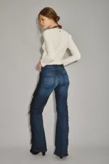 Jean de corte recto y tiro medio, color azul oscuro, con detalle de flecos negros y ojales metálicos a lo largo de la costura lateral.